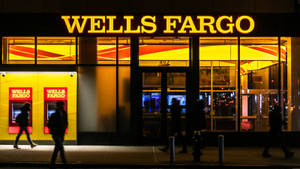 人們夜晚經過帶有黃色標誌的 Wells Fargo 銀行。 — 夜晚 壁紙