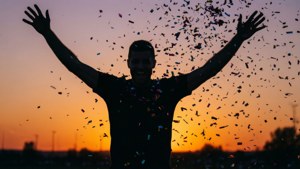 一個男人高舉雙臂慶祝，日落時分紙屑飄落。 — FIFA 世界盃 壁紙