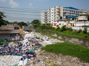 河岸被垃圾袋和廢棄紡織品覆蓋，靠近建築物。 — 4:3 壁紙