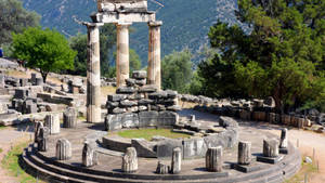 古希臘神廟遺跡，柱子和石塊周圍環繞著綠樹和山脈。 — 綠色樹木動畫 壁紙