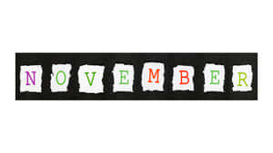 撕紙字母在黑色背景上拼出 november，顏色為紫色、綠色和橙色 — 冬季桌面 壁紙