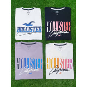綠色草地上四件折疊好的Hollister California T恤。 — Hollister 壁紙