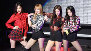 四位女K-pop表演者在燈光明亮的舞台上自信擺姿勢，穿著色彩繽紛的服裝。 — Blackpink 壁紙