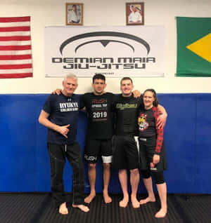 四位武術家在鋪有藍色軟墊和掛有Demian Maia柔術橫幅的健身房中一起擺姿勢。 — 終極格鬥冠軍賽 壁紙