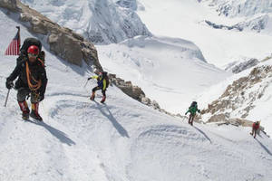 四位登山者用冰斧和繩索攀登雪山斜坡。 — 攀爬 壁紙
