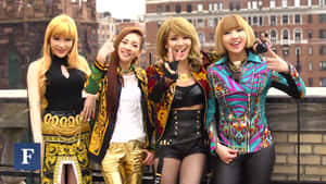 四位穿著搶眼服裝的女性在城市屋頂上快樂地擺姿勢。 — 2NE1 壁紙