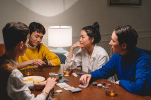 四個人圍著一張木桌玩撲克牌和籌碼，有飲料和籌碼。 — 家庭 壁紙