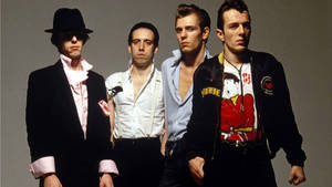 四位穿著1980年代龐克時尚的男士在工作室中嚴肅地擺姿勢 — 岩石 壁紙