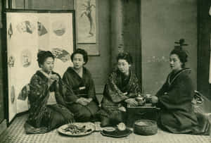 四位穿著和服的女性坐在榻榻米上，在傳統日式房間中分享茶和小吃。 — 花園 壁紙