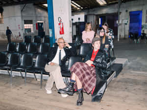 四位時尚打扮的人士在一個有黑色椅子的工業場所中擺姿勢。 — 模特兒 壁紙