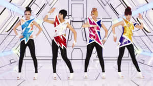 四位身穿閃電服裝的表演者在發光的未來感舞台上跳舞。 — 2NE1 壁紙