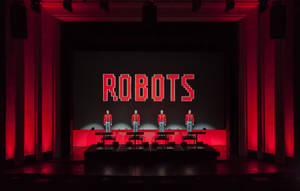 四位身穿紅色外套的演員在舞台上，身後有一個紅色發光的「ROBOTS」標誌。 — 音樂 壁紙