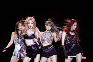 K-pop 組合在舞台上穿著閃亮服裝，擺出動感姿勢表演。 — 美學音樂 壁紙