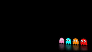 四個經典 Pac-Man 鬼魂，分別為粉紅色、藍色、橙色和紅色，在深色表面上排成一排 — 酷炫遊戲 壁紙
