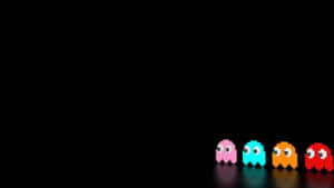 四個經典 Pac-Man 鬼魂，分別為粉紅色、青色、橙色和紅色，站在深色表面上。 — 高畫質遊戲 壁紙
