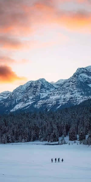 日落時分，四個人在雪山附近的冰凍湖泊上行走。 — 冬季美學 壁紙