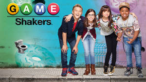 四位來自 Game Shakers 的年輕演員一起站在人行道上，背景是塗鴉。 — 遊戲玩家標誌 壁紙