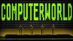 四個穿西裝的人物在講台上，發光綠色「COMPUTERWORLD」文字與二進制代碼背景。 — 音樂 壁紙