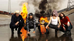 四個男人蹲在工業火車調車場的熊熊烈火旁。 — 岩石 壁紙