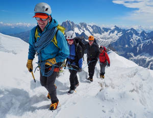 四名登山者正在攀登白雪覆蓋的山脊，身後是積雪的山峰。 — 攀爬 壁紙
