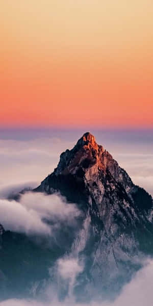 日落時分，橙色和粉紅色的天空下，山峰聳立於雲層之上。 — 山景 壁紙