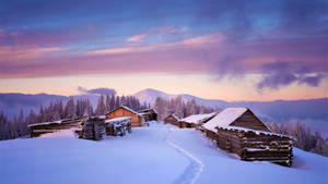 暮色中白雪覆蓋的山間小屋，天空呈現紫色和粉紅色 — 冬季風景 壁紙