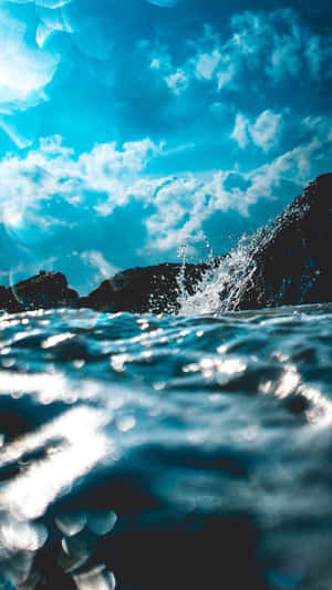 在明亮的藍天白雲下，海浪拍打著深色的岩石。 — 海洋 壁紙