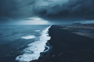 在暴風雨的天空下，深色火山沙灘上波浪拍岸。 — 海灘 壁紙