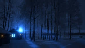 冬日森林夜晚，一間被雪覆蓋的小屋，窗戶透出光芒。 — 冬季風景 壁紙