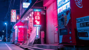 夜晚霓虹燈照亮的日本街道，商店關閉，有一台紅色自動販賣機。 — 城市燈光 壁紙