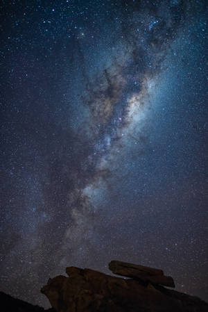 在繁星點點的夜空下，銀河系在黑色岩石剪影上方閃耀 — 岩石 壁紙
