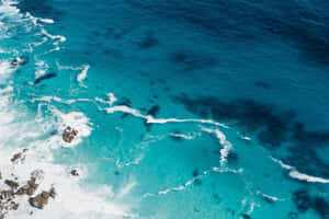 從高空視角看，碧綠海浪拍打黑色岩石。 — 海灘 壁紙