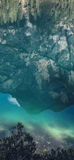 一個寧靜的山間湖泊，碧綠的湖水倒映著岩石峭壁和松樹。 — 自然 iPhone 壁紙