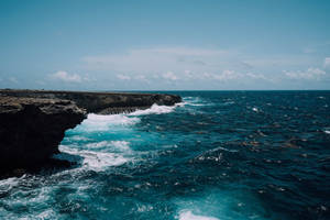 在部分多雲的天空下，碧綠的海浪拍打著深色的岩石懸崖。 — 波浪 壁紙