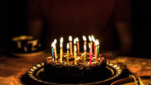 巧克力生日蛋糕，上面有點燃的蠟燭，放在裝飾盤上。 — 生日快樂蛋糕 壁紙