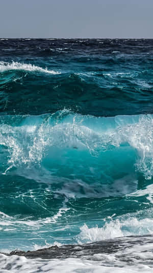 藍綠色海浪拍打在深色岩石上，濺起白色泡沫。 — 波浪 壁紙