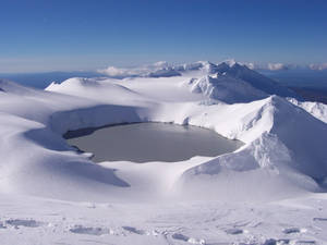 在晴朗藍天下，被群山環繞的白雪覆蓋的火山口湖。