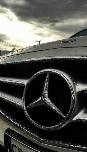 在暴風雨天空下，帶有雨滴的 Mercedes-Benz 汽車水箱護罩特寫。 — Mercedes Amg iPhone 壁紙