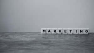 在灰色紋理表面上拼出 marketing 的白色字母瓷磚。 — 簡約暗黑美學 壁紙