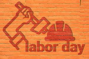 橙色磚牆上的紅色labor day塗鴉，帶有錘子和安全帽符號。 — 勞動節 壁紙