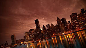 黃昏時分戲劇性的城市天際線，燈光在水面上反射。 — 紐約 壁紙