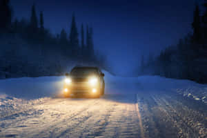 汽車在夜間行駛於積雪的森林中，車頭燈照亮道路。 — MacBook Air 壁紙
