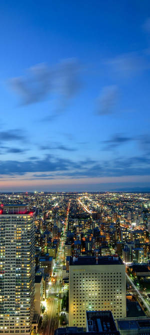 城市燈光在黃昏天空下閃爍，雲朵散佈。 — Pixel 11 壁紙