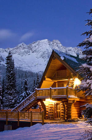 暮色中雪山裡的舒適小木屋，窗戶透出溫暖燈光。 — 冬季風景 壁紙