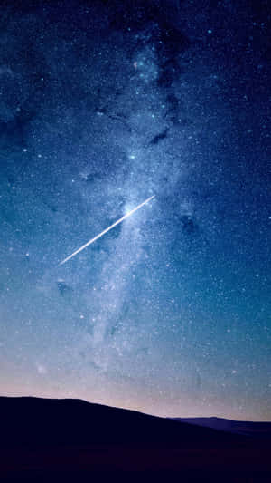 一顆明亮的流星在黑暗山丘上方的星空中留下一道軌跡。 — 夜空 壁紙