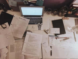 在溫暖的燈光下，一張雜亂的書桌，上面有化學文件、筆記型電腦和書寫工具。 — 書桌 壁紙