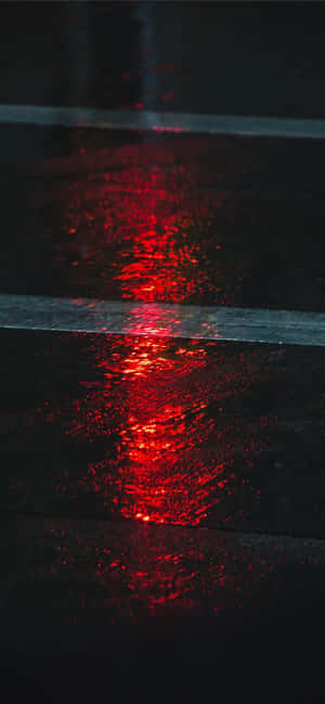 夜間，紅光照亮潮濕的道路條紋。 — iPhone 11 Pro 壁紙