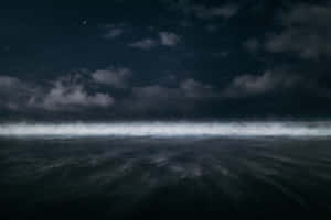 繁星夜空下的黑暗海洋，上方有霧濛濛的雲朵 — 海洋桌面 壁紙