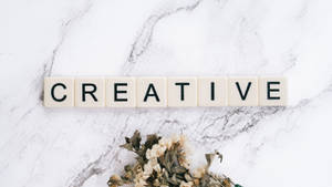 奶油色瓷磚在大理石上拼出creative，下方有乾燥花。 — 美學大理石 壁紙