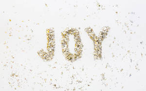 在白色表面上用金色和銀色紙屑組成的「joy」這個詞。 — 喜悅 壁紙